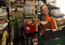 Jenny Newton, manager of the Oxfam Books and Music shop in Bedford Street, dwarfed by the piles of books they have been donated during lockdown. Picture: DENISE BRADLEY