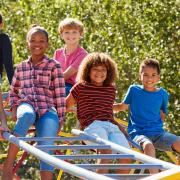 Pre-teen friends sitting on climbing frame in playground.