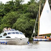 A hire cruiser passes a yacht in the Norfolk Broads